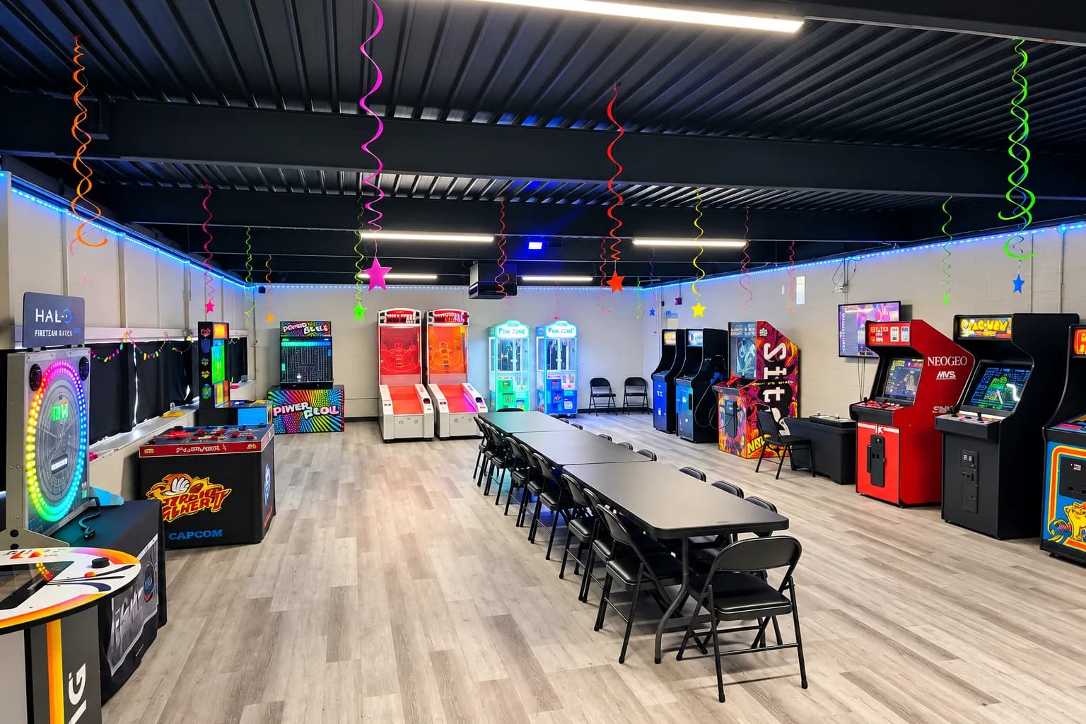 The Party Arcade Zone: arcade cabinets along the walls, a long party table, and neon streamers overhead